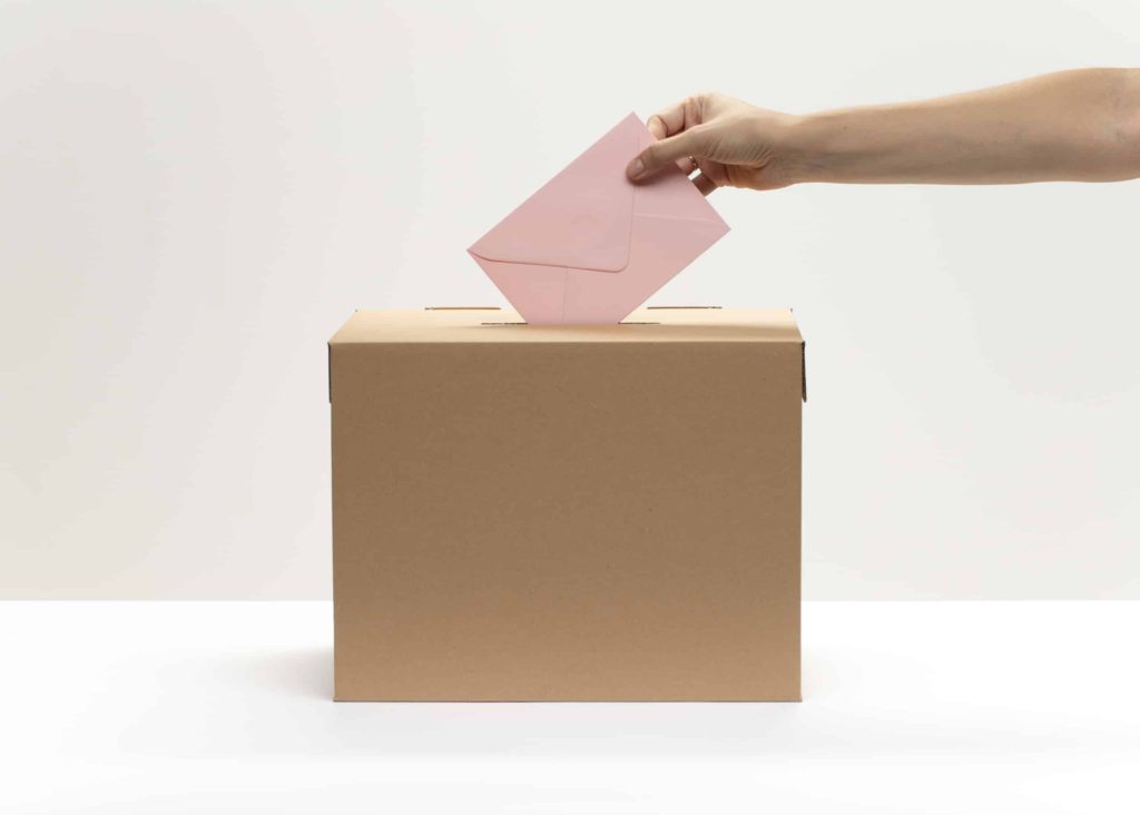 hand puts pink envelope into vote box scaled 1